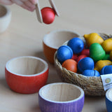 Child sorting small wooden acorns into Grapat handcrafted rainbow bowls