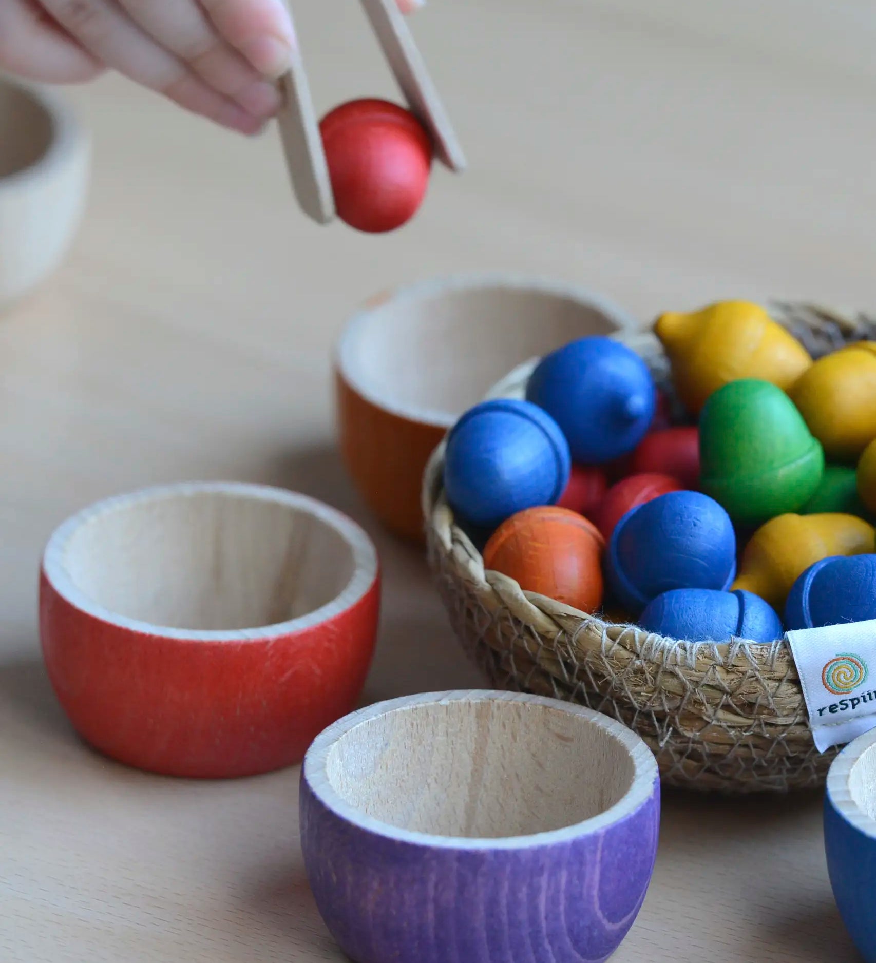 Child sorting small wooden acorns into Grapat handcrafted rainbow bowls