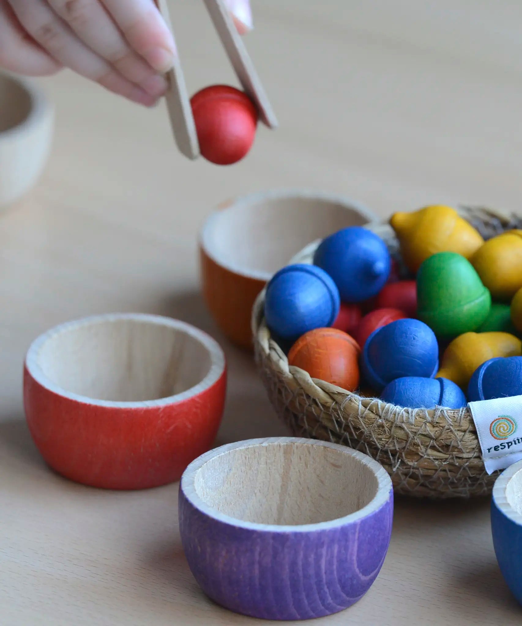 Child sorting small wooden acorns into Grapat handcrafted rainbow bowls
