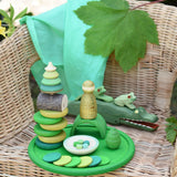 Green Grapat rainbow dish placed on a child's chair with green toys placed on it and on the chair. 