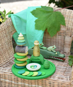 Green Grapat rainbow dish placed on a child's chair with green toys placed on it and on the chair. 