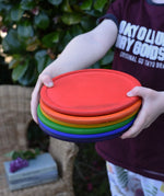 Grapat rainbow dishes stacked in a child's hands. 