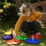 Grapat rainbow dishes placed on the grass, a child kneeling behind them placing animal crew peg dolls on the plates. 