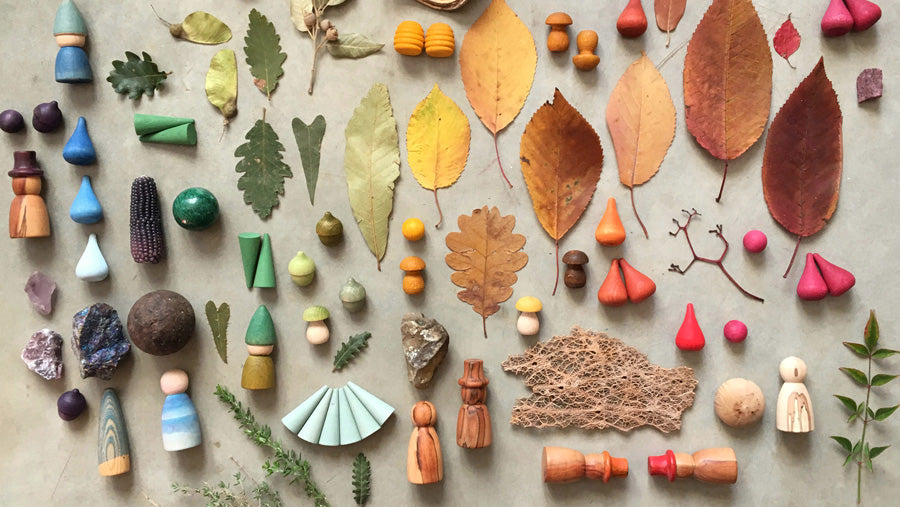A beautiful display of  mixture of Grapat wooden toys, such as nins and mandala pieces, as well as natural elements like leaves and crystals, in a cascading rainbow design.
