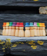 Grapat 12 Magos Rainbow Hats placed on slate. Natural wooden magos peg dolls with hand-painted rainbow coloured hats.