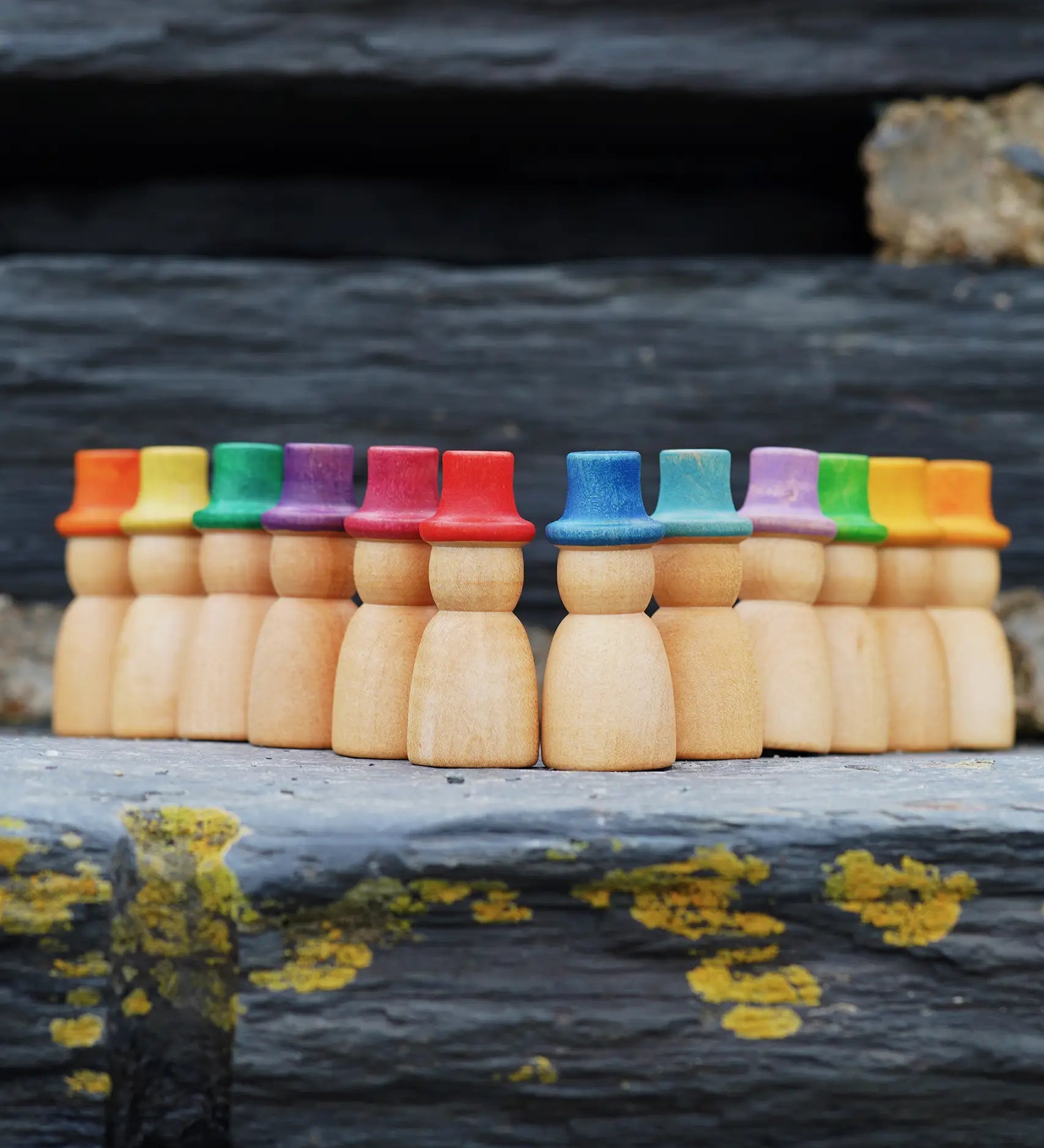Grapat 12 Magos Rainbow Hats placed on slate. Natural wooden magos peg dolls with hand-painted rainbow coloured hats.