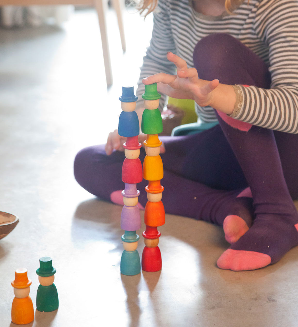 A close up of a child stacking the Grapat 12 Magos wooden peg dolls on top of each other. These wooden toys are part of a wide range of open ended toys available at Babipur.  