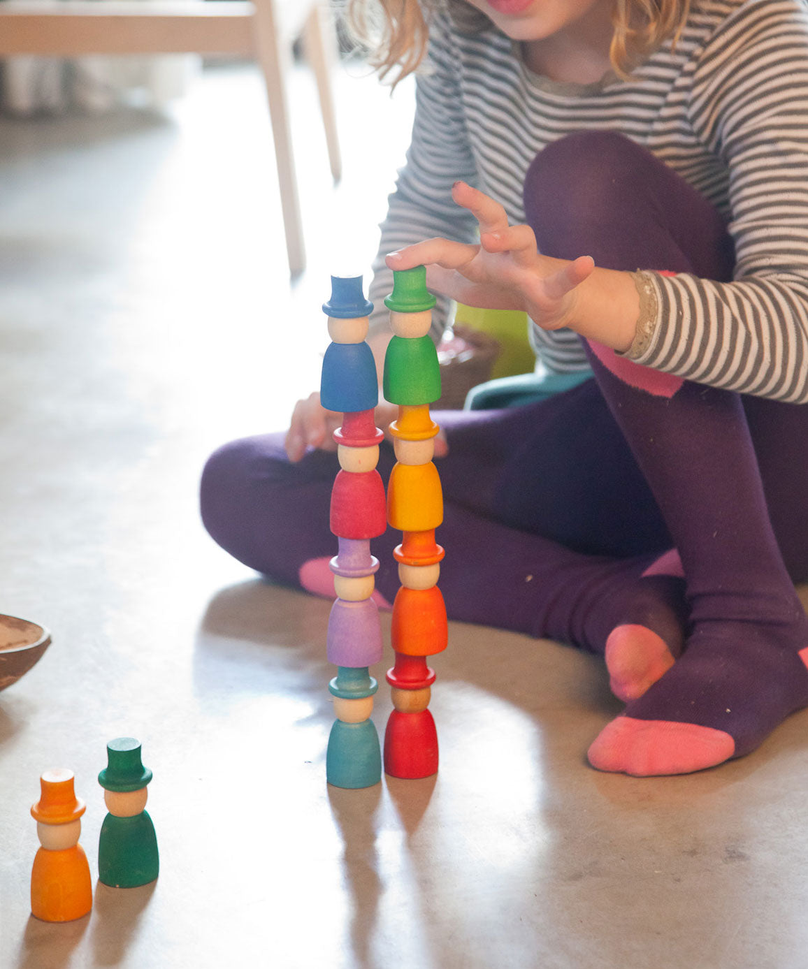 A close up of a child stacking the Grapat 12 Magos wooden peg dolls on top of each other. These wooden toys are part of a wide range of open ended toys available at Babipur.  