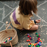 A child playing with the Grapat rainbow flowers mandala pieces. A basket can be seen filled with pieces and some are scattered on the floor around the child. 