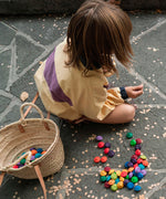 A child playing with the Grapat rainbow flowers mandala pieces. A basket can be seen filled with pieces and some are scattered on the floor around the child. 