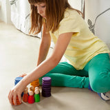 Child stacking Grapat handcrafted coloured wooden coins on a concrete surface 