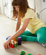 Child stacking Grapat handcrafted coloured wooden coins on a concrete surface 