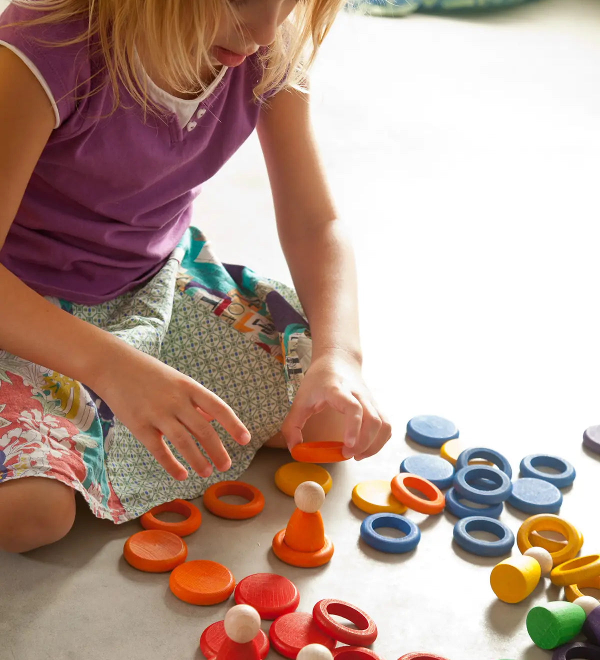 Child creative play using Grapat's coloured wooden disks, rings and peg dolls on a concrete surface