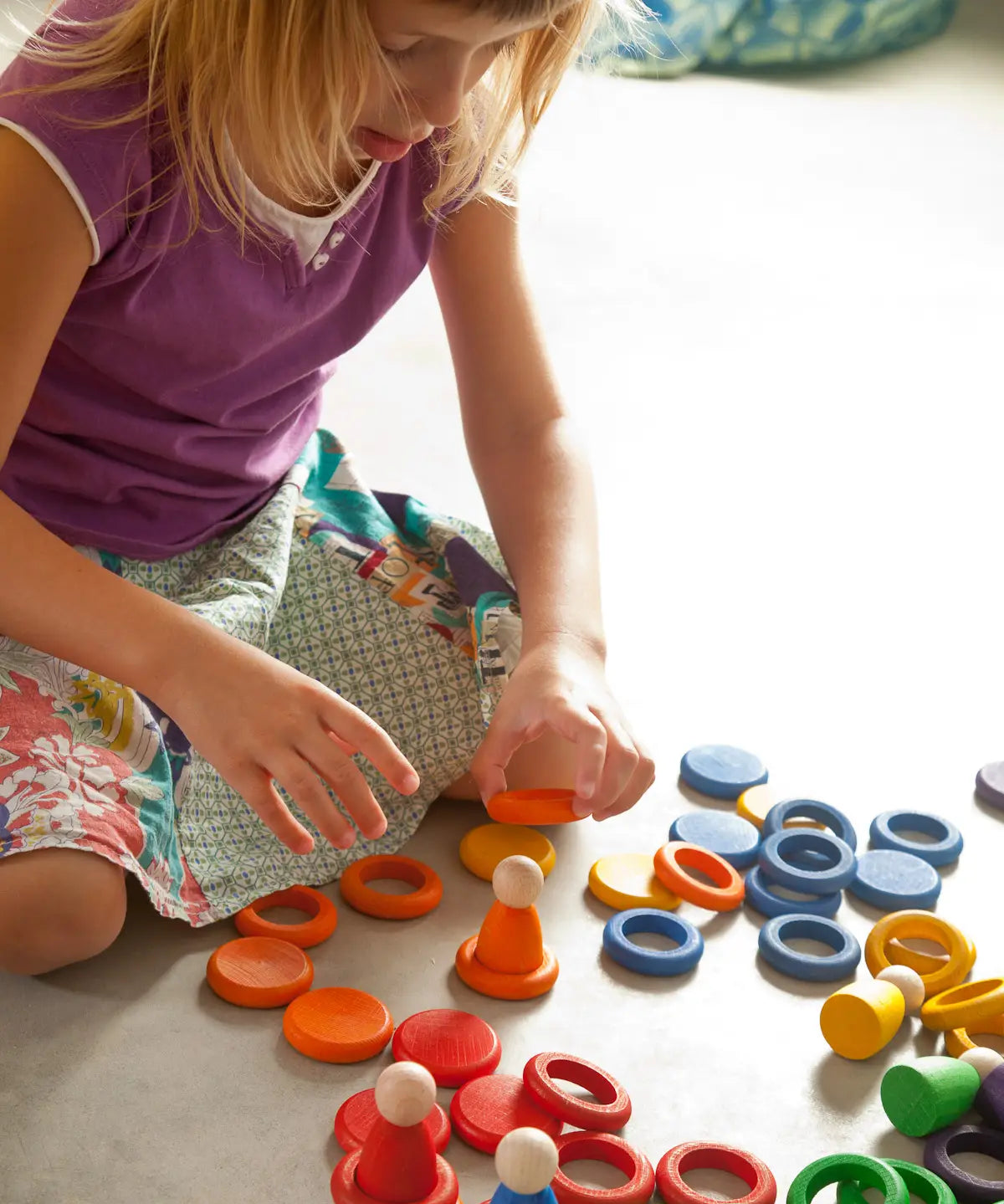 Child creative play using Grapat's coloured wooden disks, rings and peg dolls on a concrete surface