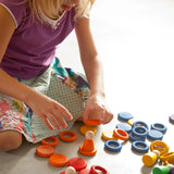 Child creative play using Grapat's coloured wooden disks, rings and peg dolls on a concrete surface