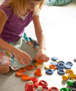 Child creative play using Grapat's coloured wooden disks, rings and peg dolls on a concrete surface
