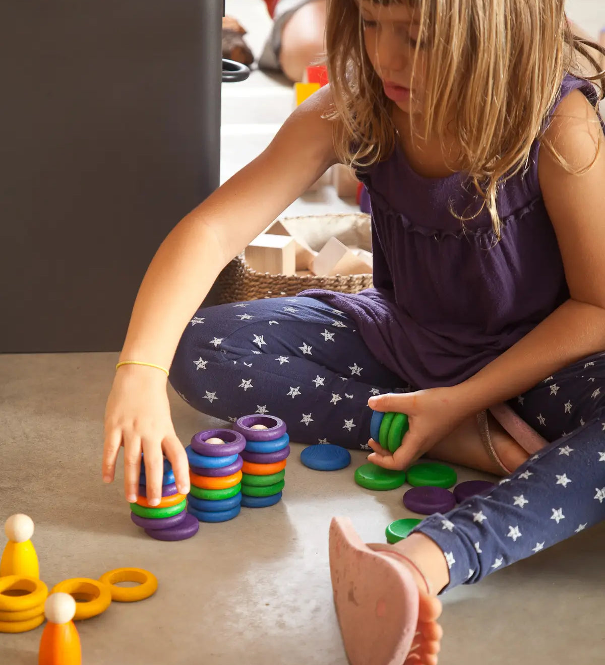 Child stacking Grapat handcrafted coloured wooden rings on a concrete surface 