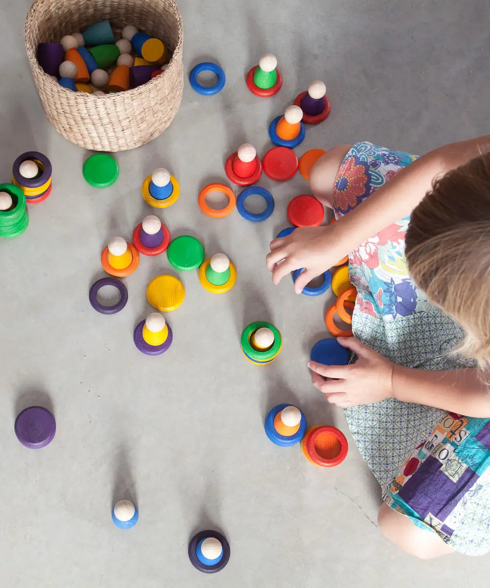 Child playing Grapat handcrafted coloured wooden rings and disks on a concrete surface 