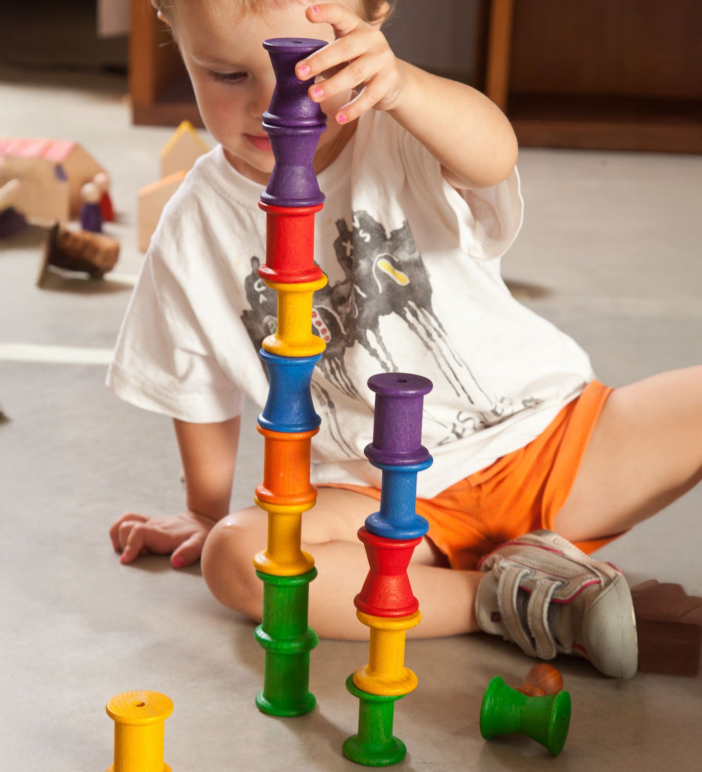 A child stacking the Grapat 18 Wooden rainbow coloured Spools on top of each other. These wooden toys are part of a wide range of open ended toys available at Babipur.  
