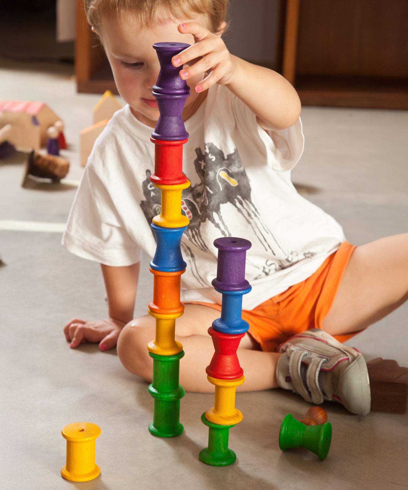 A child stacking the Grapat 18 Wooden rainbow coloured Spools on top of each other. These wooden toys are part of a wide range of open ended toys available at Babipur.  