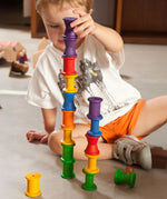 A child stacking the Grapat 18 Wooden rainbow coloured Spools on top of each other. These wooden toys are part of a wide range of open ended toys available at Babipur.  
