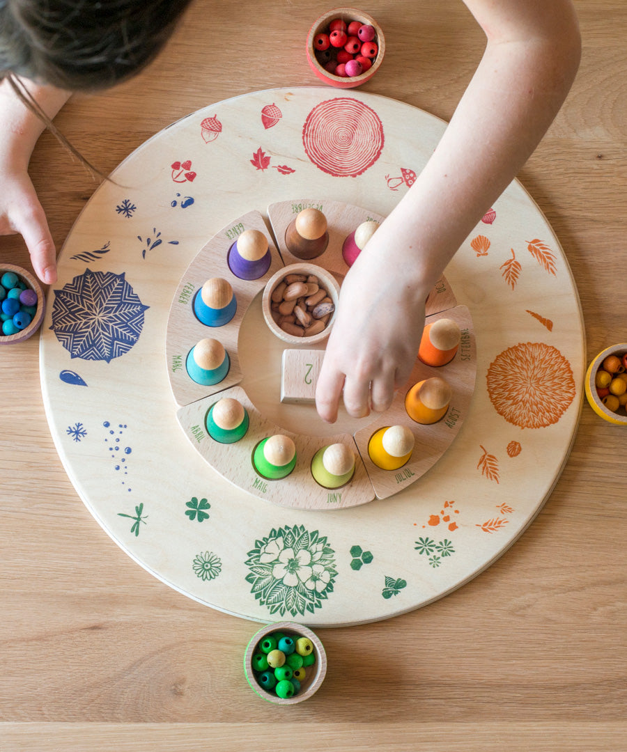 A child placing pieces from teh Grapat perpetual calendar on the Grapat 4 Seasons and Elements Play Platform. A wooden circle shaped platform and stamped with elements and details to represent the four season. These handcrafted items from Grapat are part of a wide range of wooden toys available here at Babipur.