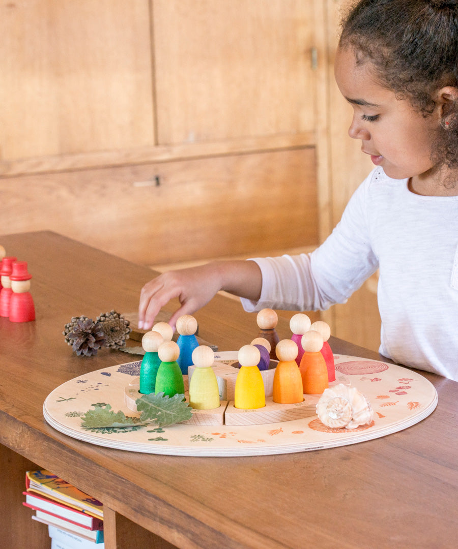 A child placing Nins from the Grapat perpetual calender on the Grapat 4 Seasons and Elements Play Platform. A wooden circle shaped platform and stamped with elements and details to represent the four season. These handcrafted items from Grapat are part of a wide range of wooden toys available here at Babipur.