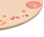 A close up of the red details on the Grapat 4 Seasons and Elements Play Platform. A wooden circle shaped platform and stamped with elements and details to represent the four season. These handcrafted items from Grapat are part of a wide range of wooden toys available here at Babipur.