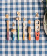 Grapat Sensory Play Tools wooden toy set. The play tools are placed on a blue and white gingham tablecloth.