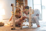 2 children on a stone floor playing with the Grapat woodland set. Showing the tubes and planks stacked into a small world setup with a combination of different Grapat wooden loose parts.