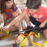 2 children playing with Grapat's wooden house blocks with coloured peg dolls on a concrete surface