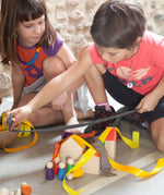 2 children playing with Grapat's wooden house blocks with coloured peg dolls on a concrete surface