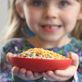 Child holding  red dish from the Grapat sorting pot set in their hands. The dish is filled with dried pulses. 