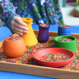 Child playing with the Grapat sorting pots wooden rainbow coloured pots filled with coloured rice.