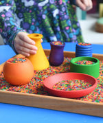 Child playing with the Grapat sorting pots wooden rainbow coloured pots filled with coloured rice.