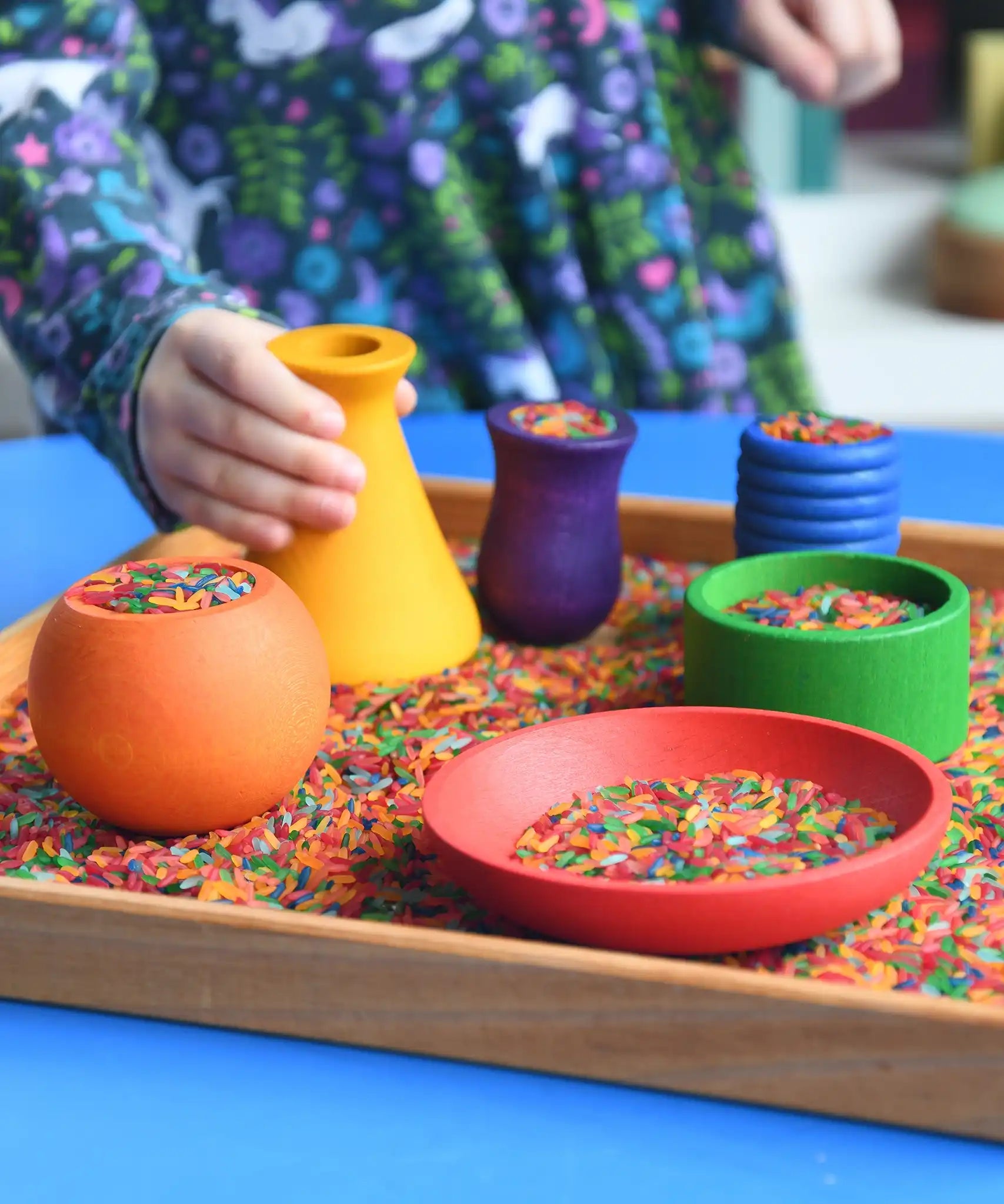 Child playing with the Grapat sorting pots wooden rainbow coloured pots filled with coloured rice.