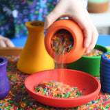Child playing with the Grapat sorting pots pouring coloured rice from an orange pot to a red dish.