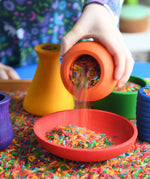 Child playing with the Grapat sorting pots pouring coloured rice from an orange pot to a red dish.