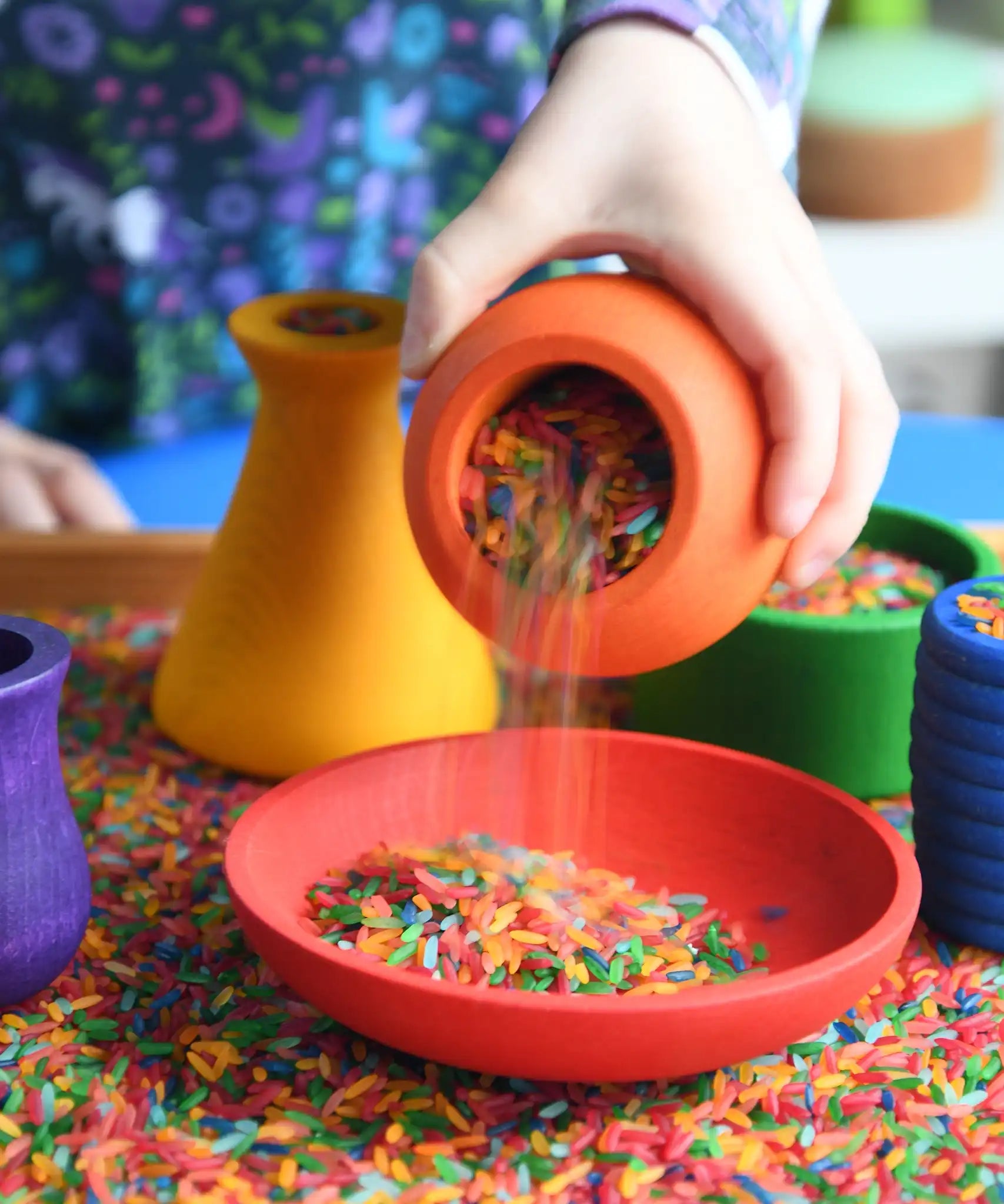 Child playing with the Grapat sorting pots pouring coloured rice from an orange pot to a red dish.