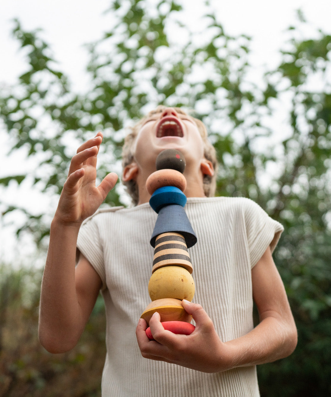 Child standing outside holding the pieces from the Grapat serendipity set showing the different handcrafted shaped pieces. Features a brown, light pink, blue yellow orange and striped pieces. 