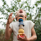 Child standing outside holding the pieces from the Grapat serendipity set showing the different handcrafted shaped pieces. Features a brown, light pink, blue yellow orange and striped pieces. 