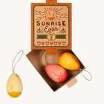 Grapat Handmade Sunrise Eggs Wooden Easter Decorations. This set includes 3 warm coloured eggs, in a range of yellows, pink and red with  hand painted floral details. The eggs are show in their cardboard packaging box.