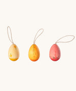 A set of three Grapat Handmade Sunrise Eggs Wooden Easter Decorations. One gg has a two tone natural and yellow painted colour, another has a two toned yellow and orange colour and the other has a pink and deep pink colour. All of the eggs have been hand painted with floral details. 