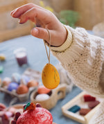 A close up of a child's hand holding the yellow coloured egg from the Grapat Handmade Sunrise Eggs Wooden Easter Decorations set.