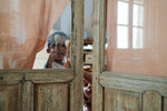 Child standing behind a wooden frame with glass holding a grey handcrafted painted Grapat puppet next to a orange handcrafted painted wooden Grapat puppet held by a sitting child