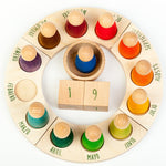 Grapat English Perpetual Calendar displaying the 12 nin peg dolls in colours representing the months of the year according to Waldorf teachings. The display ring has each month written in English around the edge and two cubes in the centre to mark the day