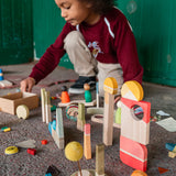 Child crouched down on the floor building towers with the Grapat happy place Waldorf toy set