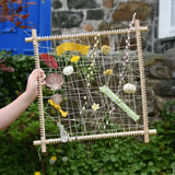 Grapat weaving frame built and filled with natural material including laves, flowers, pussy willow branches and material scraps.