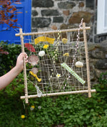 Grapat weaving frame built and filled with natural material including laves, flowers, pussy willow branches and material scraps.