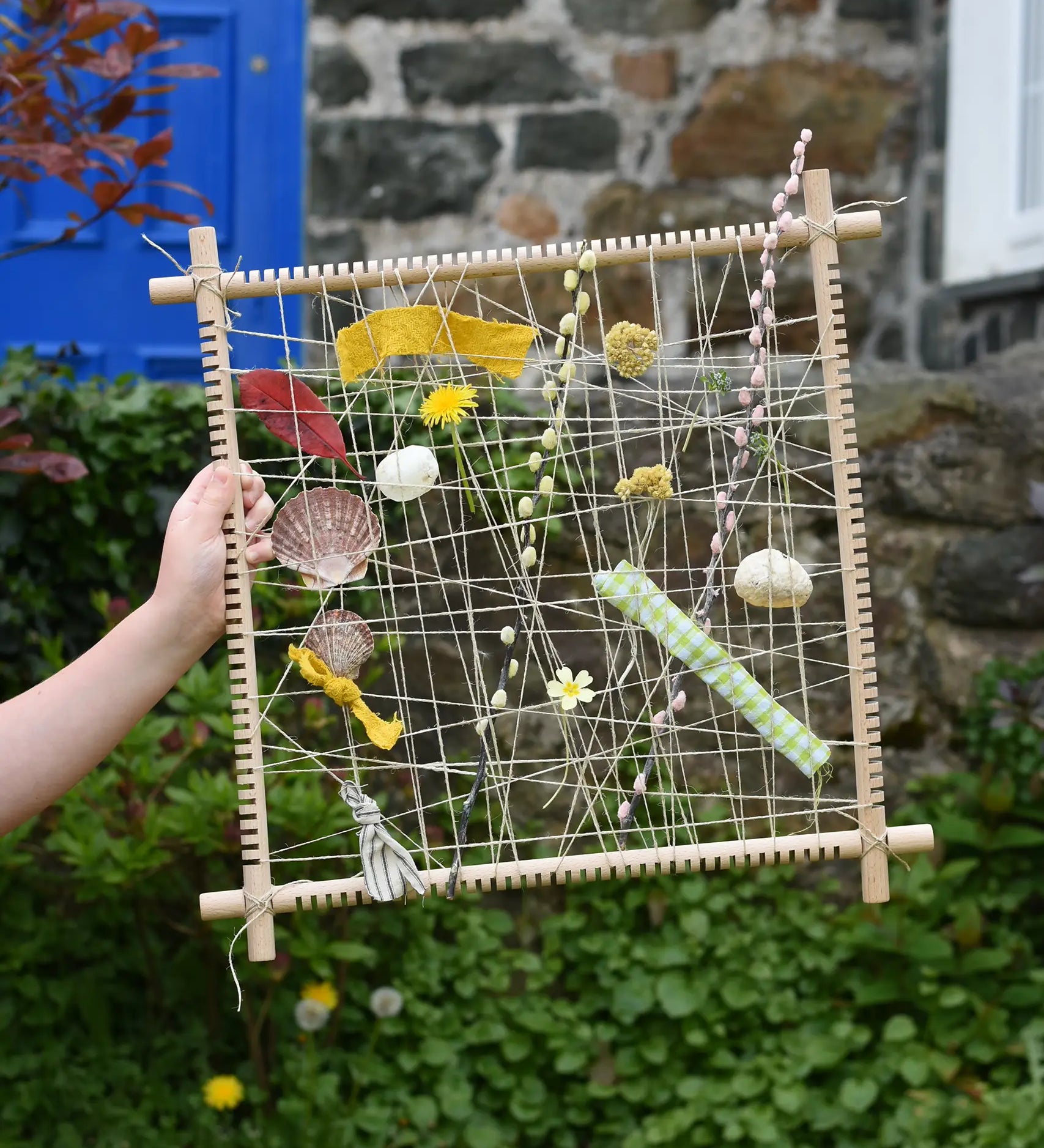 Grapat weaving frame built and filled with natural material including laves, flowers, pussy willow branches and material scraps.
